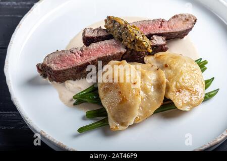 Gegrilltes Fleischsteak New York Striploin. Knödel mit Steinpilzen in Spargel-Trüffelsoße. Auf einer Holztafel auf dunklem Grund. Kopierbereich Stockfoto