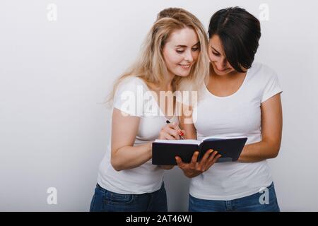 Zwei hübsche Frauen, die sich im Notizbuch notieren. Glückliche Emotionen. - Bild Stockfoto