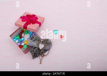Geschenk in einem rosafarbenen Kästchen auf hellrosa Hintergrund mit einem Kopierbereich. Geschenkbox für ein Mädchen mit Korbherz daneben geöffnet Stockfoto