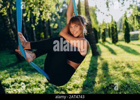 Nettes Mädchen, das im Park im Freien Yoga macht. Glücklich mit der Kamera Stockfoto