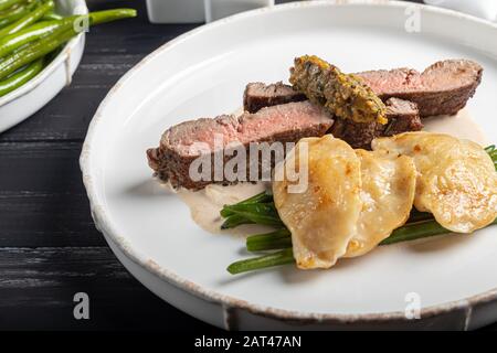 Gegrilltes Fleischsteak New York Striploin. Knödel mit Steinpilzen in Spargel-Trüffelsoße. Auf einer Holztafel auf dunklem Grund. Kopierbereich Stockfoto