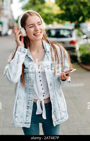 Glückliches Mädchen, das ein Smartphone hält und Musik in einem Kopfhörer hört - Bild im Freien Stockfoto