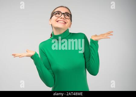 Fröhliches junges Mädchen in Brille, das im Studio posiert, zuckt überraschend und sieht auf Stockfoto