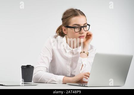 Intelligente Geschäftsfrau sitzt und arbeitet vorsichtig hinter einem Laptop mit einer Tasse Kaffee und einem ipad auf dem Tisch Stockfoto