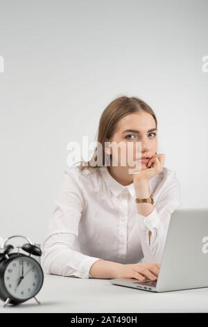 Frau sitzt am Tisch und arbeitet in einem Laptop mit Blick auf die Kamera Stockfoto