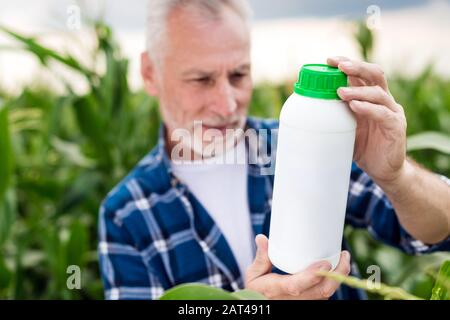 Der alte Mann auf einem Feld, der auf eine Flasche in seinen Händen blickt. Düngerflasche verspottern Stockfoto