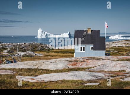 Typisches farbenfrohes blaues Fischerhaus aus Holz mit Eisberg im Gebiet der Disko-Bucht Grönland und Ilulissat. Typische Architektur im arktischen Kreis. Sommer Stockfoto