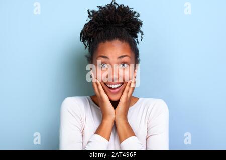 Nahaufnahme des Porträts eines hübschen Mädchens aus Mulatto über blauem Hintergrund mit verblüffter Emotion im Gesicht - Bild Stockfoto