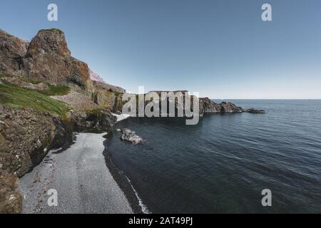 Arctic Beach mit kleinem Wasserfall in Grönland. In der Nähe des kleinen Dorfes Qeqertarsuq, Disko Island in Grönland. Blauer Himmel mit Meer und grünen Pflanzen. Stockfoto