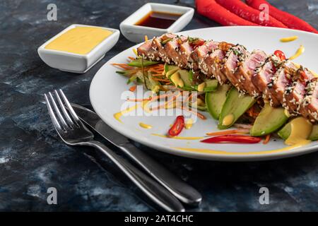 Japanische Küche. Tataki mit Thunfisch. Frittierter Fisch mit Sesamsamen und Sojasoße, Wasabi, Kalk. Auf einem Kopfkissen Gemüse. Avocados, Streifen Chilischoten Stockfoto