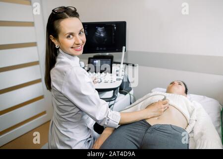 Junge lächelnde Frau Arzt Sonograph mit Ultraschallgerät während der Durchführung von Ultraschalltests des weiblichen Patienten Abdomen im Krankenhaus Stockfoto