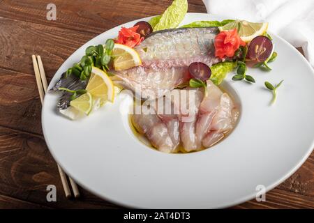 Hellgesalzenes dorado mit Sonnenblume in Trüffelöl. Neben Zitronenscheiben, Limetten, Trauben, eingepickten Ingwer. Seitlich an der Platte befinden sich Essstäbchen. Ein Stockfoto