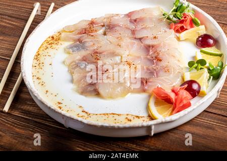 Hellgesalzenes dorado mit Sonnenblume in Trüffelöl. Neben Zitronenscheiben, Limetten, Trauben, eingepickten Ingwer. Seitlich an der Platte befinden sich Essstäbchen. Ein Stockfoto