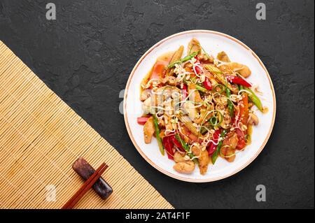 Hähnchenchop Suey in weißer Platte mit schwarzem Schieferhintergrund. Chop Suey ist ein Gericht der amerikanischen chinesischen Küche mit verschiedenen Rührgemüse, Hühnchen m Stockfoto