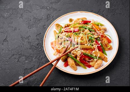 Hähnchenchop Suey in weißer Platte mit schwarzem Schieferhintergrund. Chop Suey ist ein Gericht der amerikanischen chinesischen Küche mit verschiedenen Rührgemüse, Hühnchen m Stockfoto