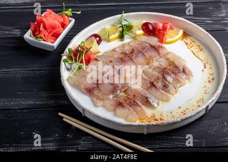 Hellgesalzenes dorado mit Sonnenblume in Trüffelöl. Neben Zitronenscheiben, Limetten, Trauben, eingepickten Ingwer. Seitlich an der Platte befinden sich Essstäbchen. Ein Stockfoto