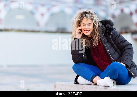 Lockig blonde Frau auf Blech sitzend. Lässige Kleidung Stockfoto