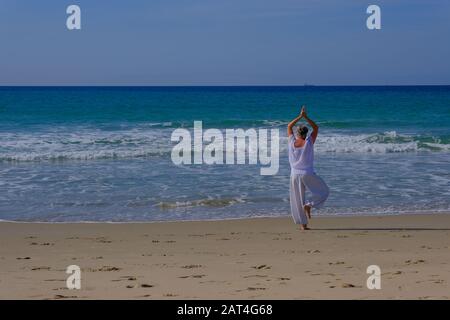 Ältere Frau mit grauem Haar, die Qi Gong und Yoga am Strand von Tarifa macht Stockfoto