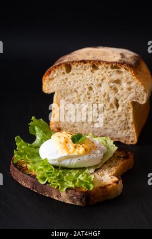 Bio Food Frühstückskonzept hausgemachtes Pochiertes Ei oder Eier benedict auf Sauerteig Brot geröstet auf schwarzem Schieferbrett Stockfoto