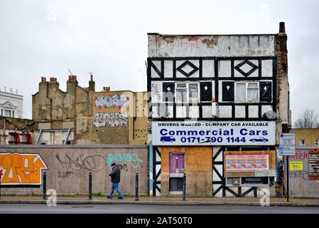 Eine männliche Figur, die an einem verlassenen, unwecklichen Gebäude vorbeiläuft, das auf den Abriss an Der Commercial Road Limehouse East London England UK wartet Stockfoto