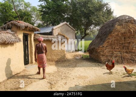 Landmann in der Nähe seiner Schlammhütte mit Blick auf Heuhaufen in einem indischen Dorf in Bolpur, Westbengalen Stockfoto