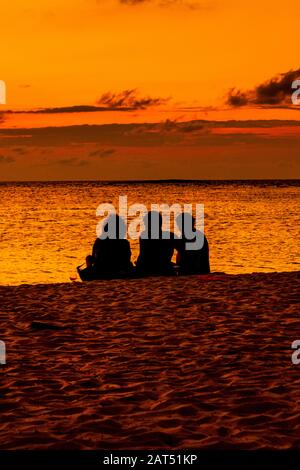 Drei Personen sitzen an einem Strand und beobachten einen karibischen Sonnenuntergang in Kuba Stockfoto