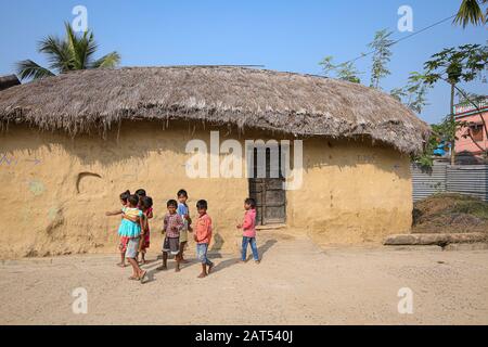 Kinder posieren für ein Foto außerhalb einer Schlammhütte in einem Stammesdorf in Bolpur, Westbengalen, Indien Stockfoto