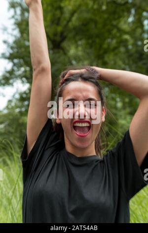 Porträt der gemischten Rasse indianerin schreit aus Freude mit im Freien erhobenen Armen. Stockfoto