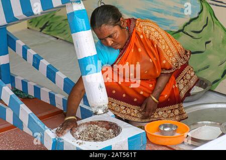 Die indische Landfrau, die Reis mit einer manuellen Maschine in einem Dorf in Bolpur in Westbengalen, Indien mahlt Stockfoto
