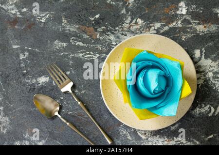 Dekorative Blume aus farbigen Papierservietten. Tischeinstellung mit farbigen Papierservietten auf Steingrund, flacher Lay. Freier Speicherplatz für Ihren Text. Stockfoto