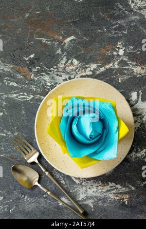 Dekorative Blume aus farbigen Papierservietten. Tischeinstellung mit farbigen Papierservietten auf Steingrund, flacher Lay. Freier Speicherplatz für Ihren Text. Stockfoto