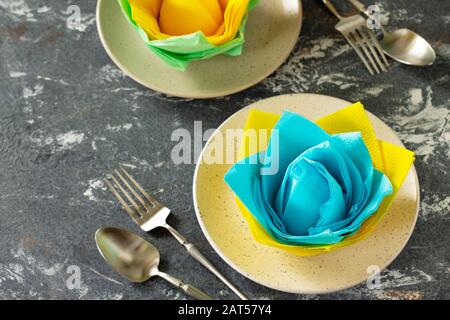 Dekorative Blume aus farbigen Papierservietten. Tischeinstellung mit farbigen Papierservietten auf Steinhintergrund. Freier Speicherplatz für Ihren Text. Stockfoto