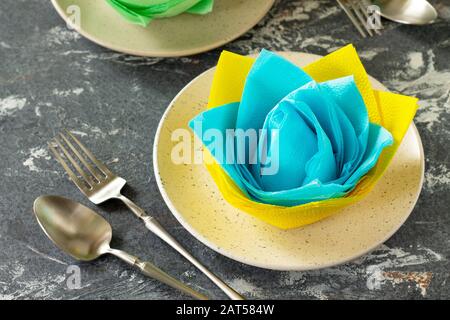 Dekorative Blume aus farbigen Papierservietten. Tischeinstellung mit farbigen Papierservietten auf Steinhintergrund. Stockfoto