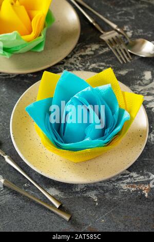 Dekorative Blume aus farbigen Papierservietten. Tischeinstellung mit farbigen Papierservietten auf Steinhintergrund. Stockfoto