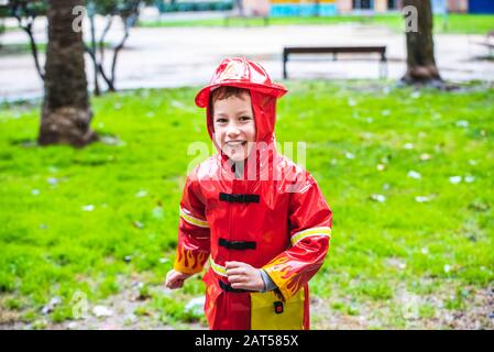 Lustige Kinder, die mit rotem Regenmantel bekleidet sind, spielen an einem regnerischen Tag in einem Park. Stockfoto