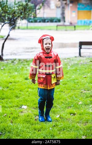 Lustige Kinder, die mit rotem Regenmantel bekleidet sind, spielen an einem regnerischen Tag in einem Park. Stockfoto