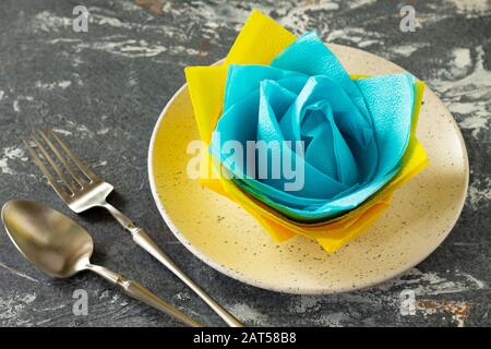 Dekorative Blume aus farbigen Papierservietten. Tischeinstellung mit farbigen Papierservietten auf Steinhintergrund. Freier Speicherplatz für Ihren Text. Stockfoto