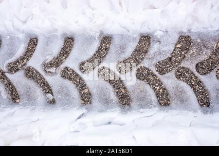 Spuren eines Traktorreifens auf verschneiten Asphalt auf einer Straße im Winter. Stockfoto