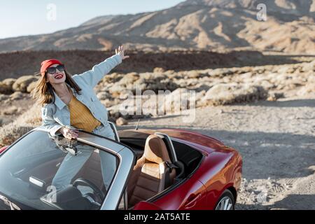 Lifestyle-Porträt einer jungen Frau, die auf der Straße im Wüstental unterwegs ist und mit der Hand aus dem Cabrio-Auto am Straßenrand kommt Stockfoto