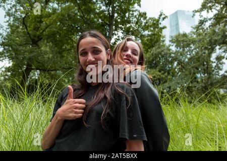 Indisches Mädchen, das mit den Daumen nach oben mit kaukasischen Mädchen steht dicht hinter und lächelt. Mittlere Aufnahme. Stockfoto