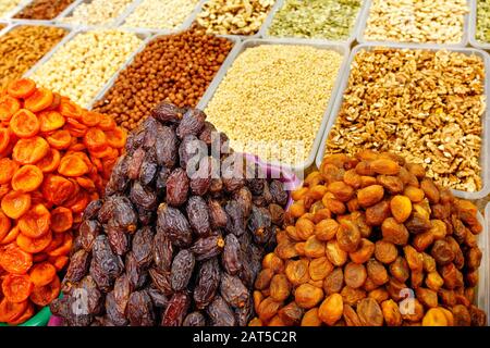 Datteln, getrocknete Aprikosen werden auf dem Markt vor dem Hintergrund verschiedener Nüsse, Mandeln, Haselnüsse, Walnüsse, Cashews in Bewegungsunschärfe verkauft. Stockfoto