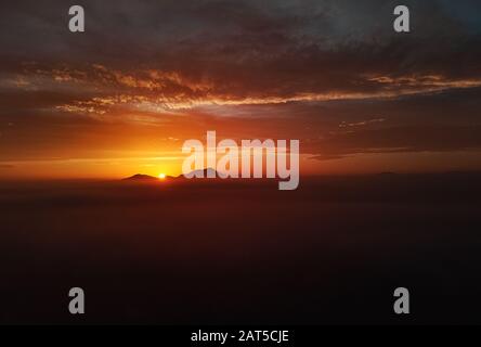 Luftbild drone Blickhorizont über Land und strahlendes helles Sonnenlicht durch die Berge, Abend malerisch orange rot bewölkt Himmel, Spanien Stockfoto