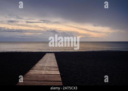 Strand von Calahonda an der Costa del Sol, Holzsteg zum Mittelmeer, flauschiger bewölkter Himmel, romantischer Morgen- oder Abendaufgang. Spanien Stockfoto