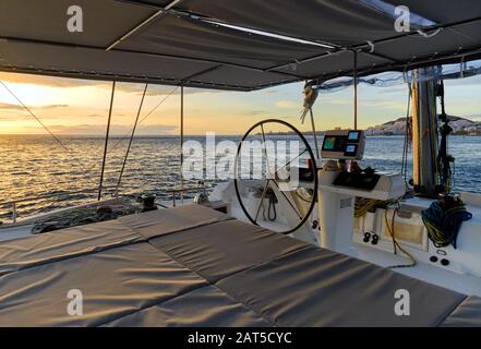 Idyllische Landschaft glühende Sonne im Ozean ruhiger Blick auf das Wasser von der offenen Terrasse der Katamatan-Flybridge, moderne Luxusyacht mit Navigations-Dashboard-Devi Stockfoto