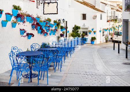 Mijas Pueblo Blanco, charmantes kleines Dorf, malerische leere Straße in der Altstadt mit hellblauen Tischen Stühle des lokalen Cafés, Blumentöpfe hängen an Stockfoto