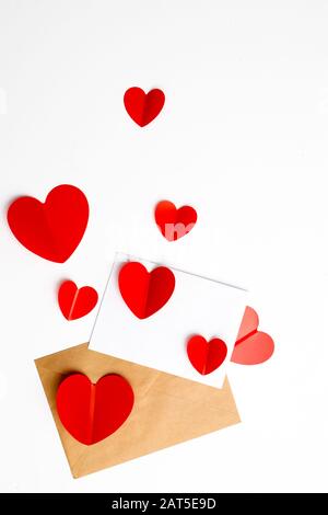 Grußkarte zum Valentinstag. Umschläge auf weißem Hintergrund und rote Kunststoffherzen. Kopierbereich. Stockfoto