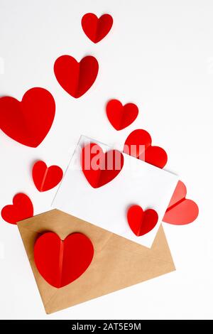 Grußkarte zum Valentinstag. Umschläge auf weißem Hintergrund und rote Kunststoffherzen. Kopierbereich. Stockfoto