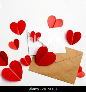 Grußkarte zum Valentinstag. Umschläge auf weißem Hintergrund und rote Kunststoffherzen. Kopierbereich. Stockfoto