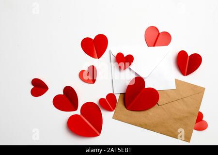 Grußkarte zum Valentinstag. Umschläge auf weißem Hintergrund und rote Kunststoffherzen. Kopierbereich. Stockfoto