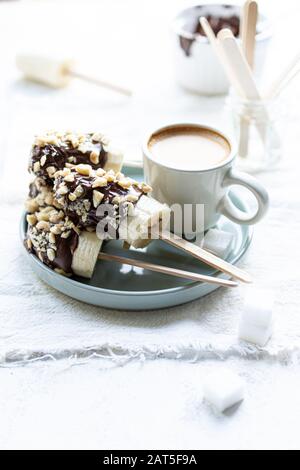 Bananen in Schokolade mit Nüssen und Morgenkaffee bestreut.Köstliche Speisen und Getränke.Lollypop Stockfoto